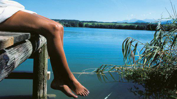 Frau lässt am Steg vor Starnberger See die Beine baumeln