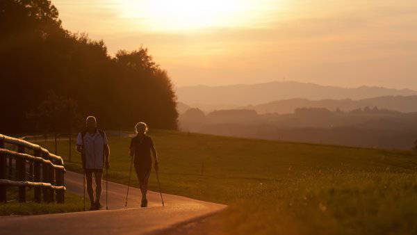 Two people are Nordic Walking on a trail in front of a beautiful misty scenery of meadows and hills