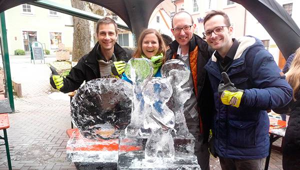 Four happy people standing in front of a handcarved ice sculpture