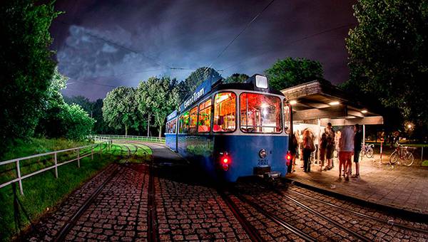 Blue tram holding at a stop with people at nighttime