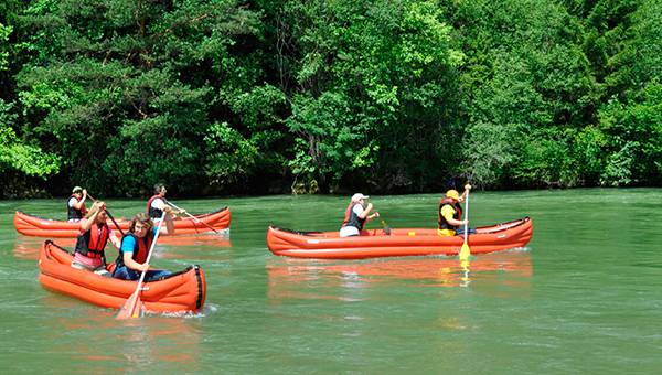 Three canoes with two people each floating on river Isar in front of green scenery