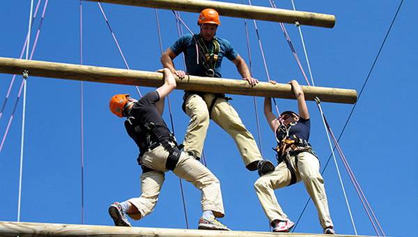 Three men climing and helping each other on high ropes course