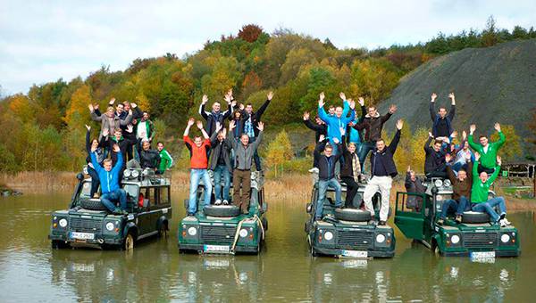 Four jeeps in water with five people each standing on top cheering