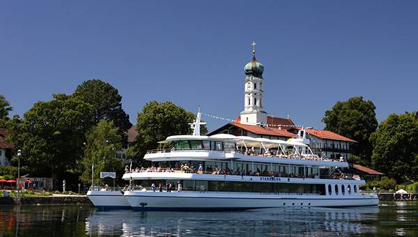 Ausflugsschiff legt am Seeufer ab, Kirche mit Zwiebelturm im Hintergrund