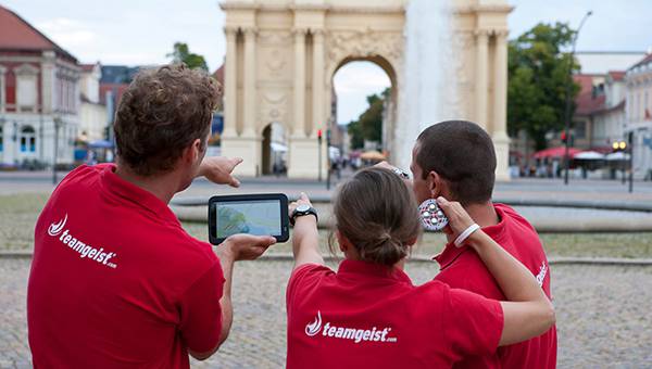 Three people looking at a tablet in front of a place of interest