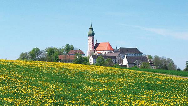 Andechs monastery in front of green grass with yellow flowers and blue sky
