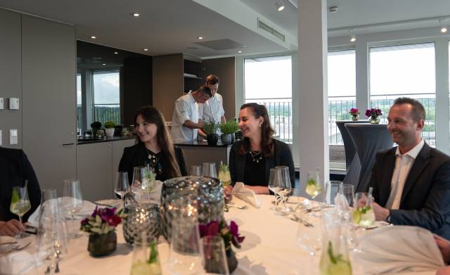 Personen am Tisch reden und lachen, während zwei Köche an Live-Cooking-Station Gerichte zubereiten